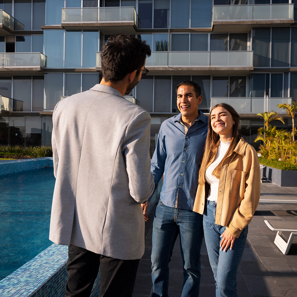 A man and a couple stand by a pool, promoting condos for rent in a sunny outdoor setting.