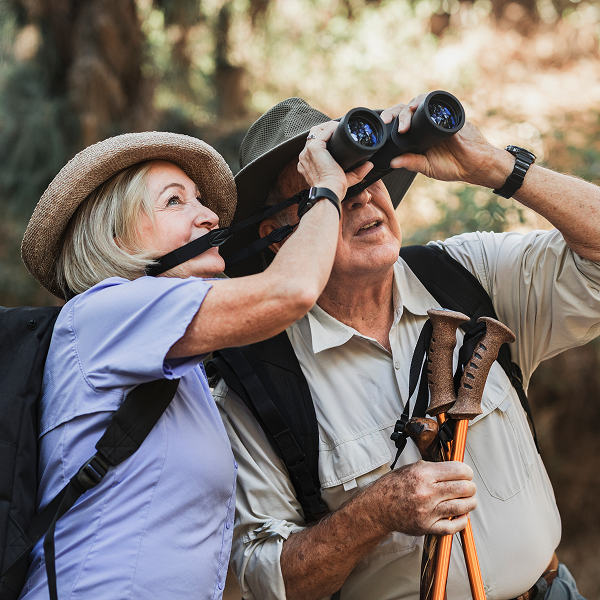 An older couple hiking, using binoculars to observe the scenery around them.