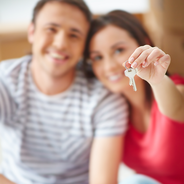 Un homme et une femme assis par terre, tenant une clé, avec un panneau indiquant "condo à louer" en arrière-plan.